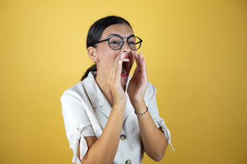 Beautiful woman over yellow background shouting and screaming loud to side with hands on mouth