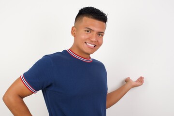 Young handsome hispanic man wearing casual t-shirt standing over white isolated background feeling happy and cheerful, smiling and welcoming you, inviting you in with a friendly gesture