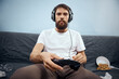 © SHOTPRIME STUDIO - Man sitting on sofa wearing headphones with gamepad playing food leisure technology lifestyle