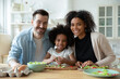 © fizkes - Portrait of happy mixed race couple with small girl cooking in kitchen. Smiling young handsome caucasian man enjoying preparing food with african ethnicity wife and adopted little biracial daughter.
