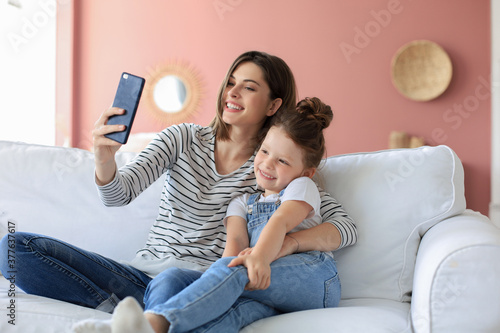 Fotomural Beautiful young mother and her little daughter taking a selfie with a smartphone at home on the couch