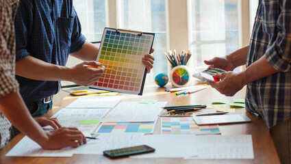 Designers hold color swatches and discuss with colleagues to design web site layouts and mobile applications.