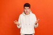 © khosrork - What do you want from me? Confused young man in stylish sweatshirt with hood spreading hands, uncomfortable situation. Indoor studio shot isolated on orange background