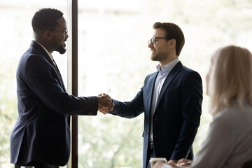 Poster - Smiling businessman handshake male colleague congratulate with job promotion or work success. Happy diverse business partners shake hands get acquainted greeting or close deal at meeting in office.