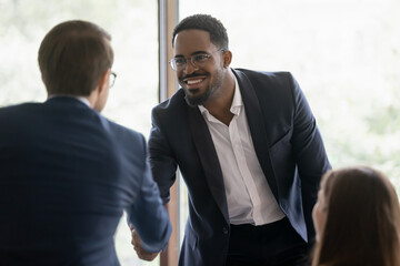 Wall Mural - Happy diverse businessmen shake hands greeting get acquainted at business meeting in office. Smiling multiracial male partners or colleagues handshake close deal after successful negotiation.
