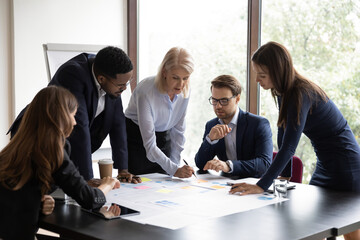 Wall Mural - Focused multiracial businesspeople brainstorm analyze company financial documents at meeting together. Concentrated diverse colleagues talk discuss business project paperwork at briefing in office.