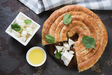 Wall Mural - Above view of sliced spanakopita or greek spiral spinach and feta cheese pie, horizontal shot on a brown stone background