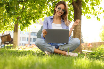 Wall Mural - Happy young woman with laptop sitting on green grass in park