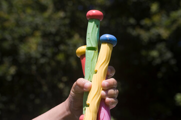 active hand of a children holding bars of a pool water game with forest background