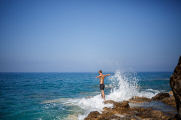 A young man stands on the rocks overlooking the open Mediterranean Sea. A guy on a warm summer sunny day looks at the sea breeze