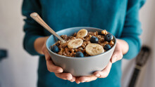 Close up of hands of woman holding homemade granola in a plate with nuts, honey, blueberries, banana and other natural ingredients, Focus on a bowl
