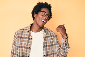 Handsome african american man with afro hair wearing casual clothes and glasses pointing thumb up to the side smiling happy with open mouth