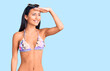© Krakenimages.com - Young beautiful latin girl wearing bikini and sunglasses very happy and smiling looking far away with hand over head. searching concept.