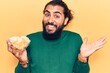 © Krakenimages.com - Young arab man holding potato chip celebrating achievement with happy smile and winner expression with raised hand