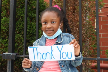 Child holding Thank You Sign outdoors with surgical mask pulled down