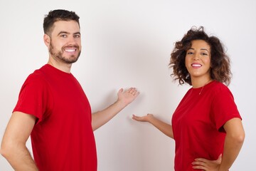 Young beautiful couple wearing red t-shirt on white background feeling happy and cheerful, smiling and welcoming you, inviting you in with a friendly gesture