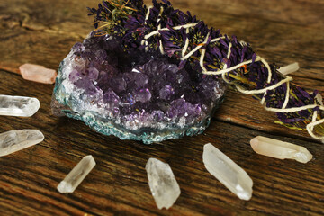 Wall Mural - A close up image of an amethyst geode and lilac smudge stick with clear quartz crystals on a dark wooden desk top. 