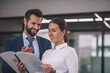 © zinkevych - Brown-haired female with bearded male colleague reading papers, smiling