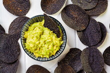 Black Potato Chips With Avocado Dip - Guacamole, White Background, Top View. Vegan Food Concept.