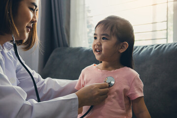 Confident asian woman healthcare professional visit her patient using a stethoscope during a young female patient well check at home.