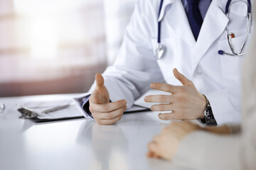 Unknown male doctor and patient woman discussing something while sittingin a darkened clinic, glare of light on the background. Close-up of hands