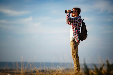 Guy looking at binoculars in hill. man in t-shirt with backpack.