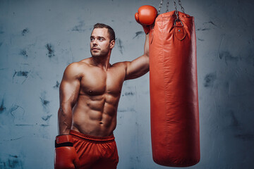 Wall Mural - Bodybuilder with huge biceps perfect abs and with protective gloves doing workout with punching bag.