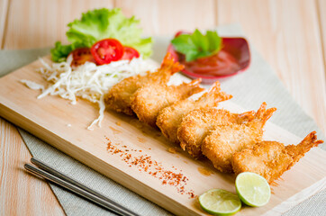 Butterfly ebi furai shrimp served with tomato and lettuce on a wooden chopping board along with ketchup