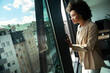 © NDABCREATIVITY - Beautiful african business woman looking outside window in office