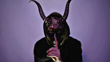 A Person Wearing A Horned Mask Isolated On A Purple Lit Background.