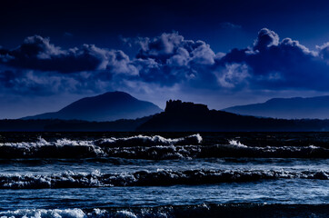 Wall Mural - Island of Procida, Campania region, Italy. Image of the island with a castle silhouette seen from a beach with nocturnal and dreamy atmosphere and mood.