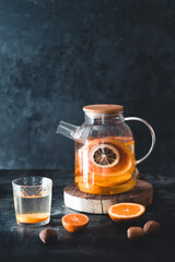 Wall Mural - Citrus tea in a transparent teapot on a dark concrete background. Healthy drink, vegan, eco product.