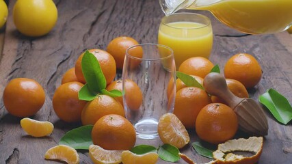 Wall Mural - Tangerine fresh is poured into a glass from a decanter. Around are ripe tangerines with leaves on an old wooden surface.