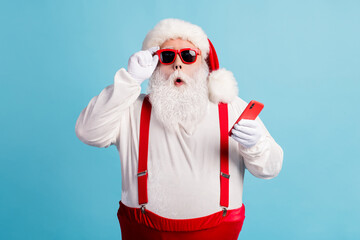 Poster - Photo of pensioner grandfather grey beard hold telephone read fake news christmas cancelled wear santa x-mas red costume suspenders sunglass white gloves cap isolated blue color background