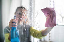 Young woman cleaning window at home using spray detergent and rag