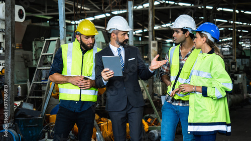Industrial engineer and businessman in suite and safety helmet working in factory, planning, discussing and training workers with tablet in metalwork place , teamwork and team concept