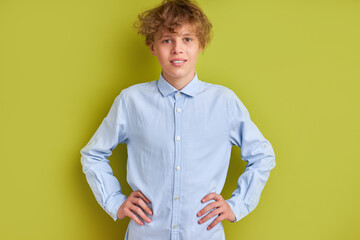 unperturbed caucasian boy isolated over green background, kid boy 14-15 years old in blue shirt look at camera