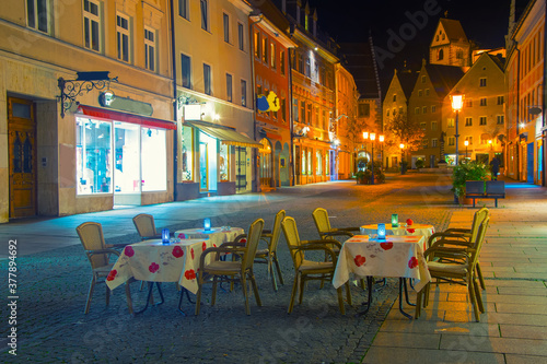 Plakat Romantic night scene of street cafe with two tables and old street with citylights on background, Fussen, Germany
