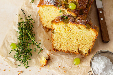 Wall Mural - Delicious homemade grape loaf cake with thyme and sugar powder on parchment paper. Light stone background.