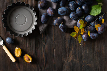 Wall Mural - Autumn cooking theme with pie pan and  plum on dark wooden background