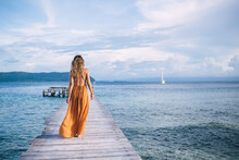 Back View Of Female Tourist Enjoying Resort Vacations In Paradise Nature Environment, Woman In Stylish Sundress Walking At Pier Recreating During Solo Travelling For Visiting Bora Bora Island