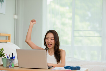 Asian young woman celebrating with laptop after success job feeling so happy and cheerful at home,Small Business Startup concept