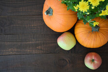 Two Apples, Two Orange And Yellow Chrysanthemums Flowers Pumpkins On Background Of Old Brown Wooden Board. Autumn Harvest, Thanksgiving Day Or Halloween Concept. Flat Lay With Copy Space.