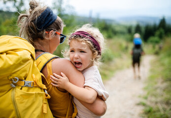 Wall Mural - rear view of mother with small crying daughter hiking outdoors in summer nature.