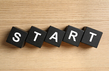 Word START made with black cubes on wooden background, flat lay