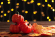 Orange pumpkins and fall leaves on the wooden table with garland yellow lights on the black wall