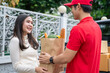 © godji10 - Selective Focus of smiling woman receiving a grocery bag from the courier. A delivery man bringing fresh food packages to customer on a business day. Online shopping, food delivery service concept.