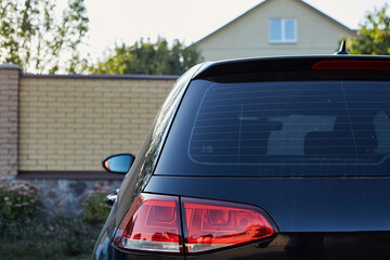 Back window of black car parked on the street in summer sunny day, rear view. Mock-up for sticker or decals