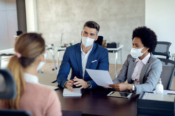 Business coworkers wearing face masks while talking to potential job candidate in the office.