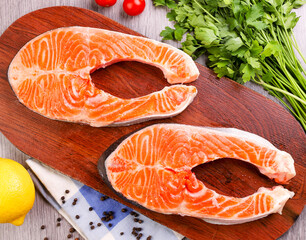 Raw salmon steak with lemon, pepper and herbs on a wooden board. Food background. Top view